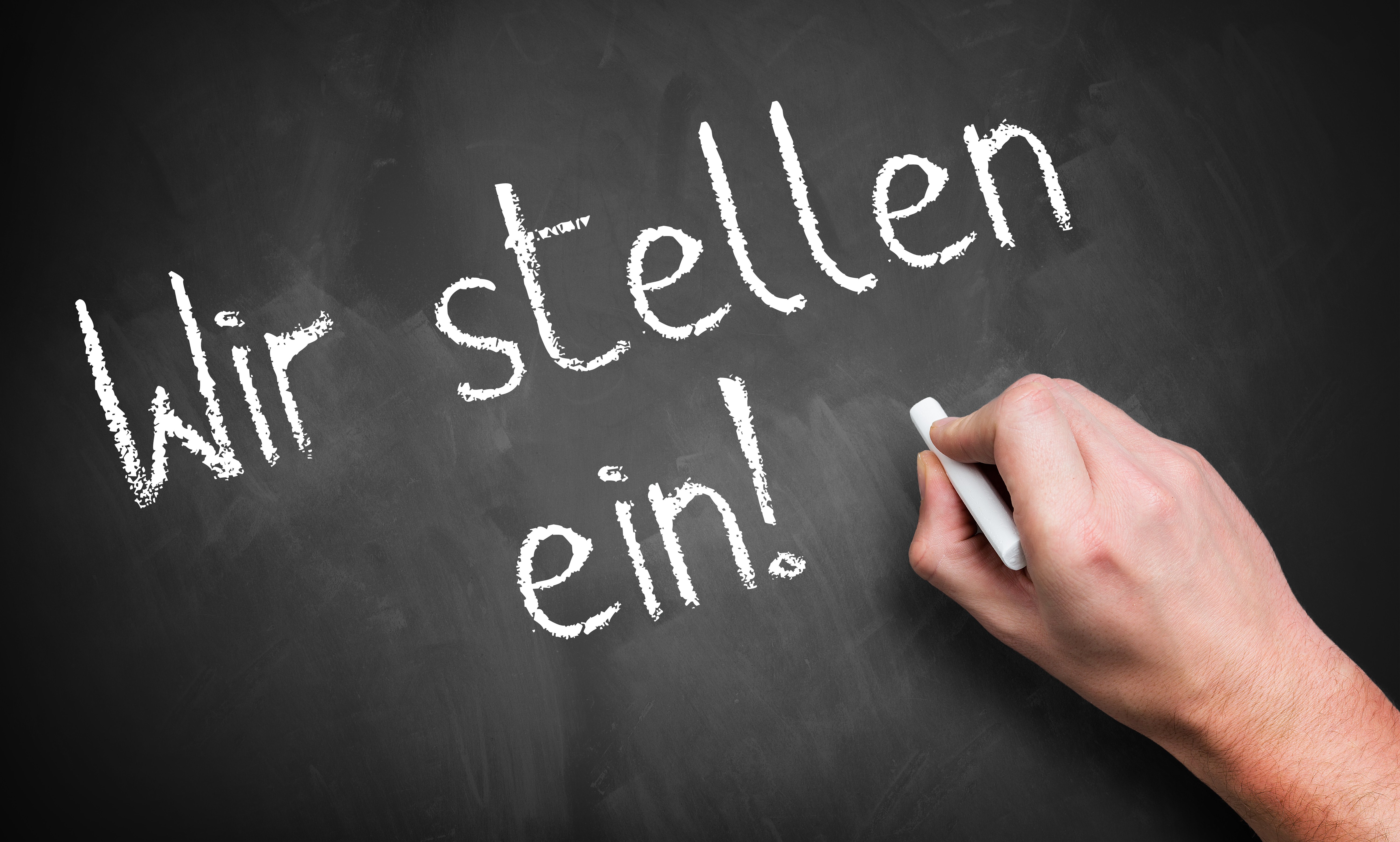 hand writing 'We are hiring!' in German on a chalkboard