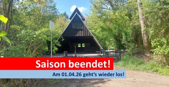 Blick auf eine Grillhütte, davor ein Textbalken, auf dem in weißer Schrift auf rotem Grund steht "Saison beendet!"