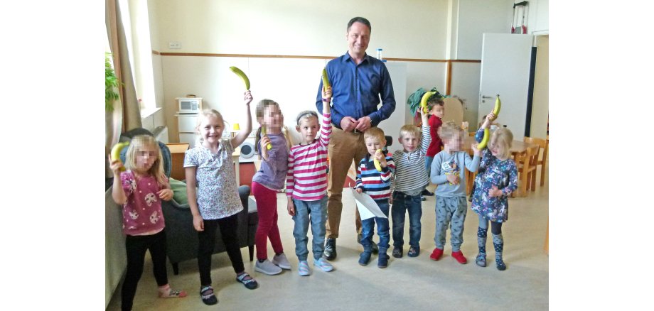 Acht Kinder und ein Erwachsener, die Bananen hoch halten