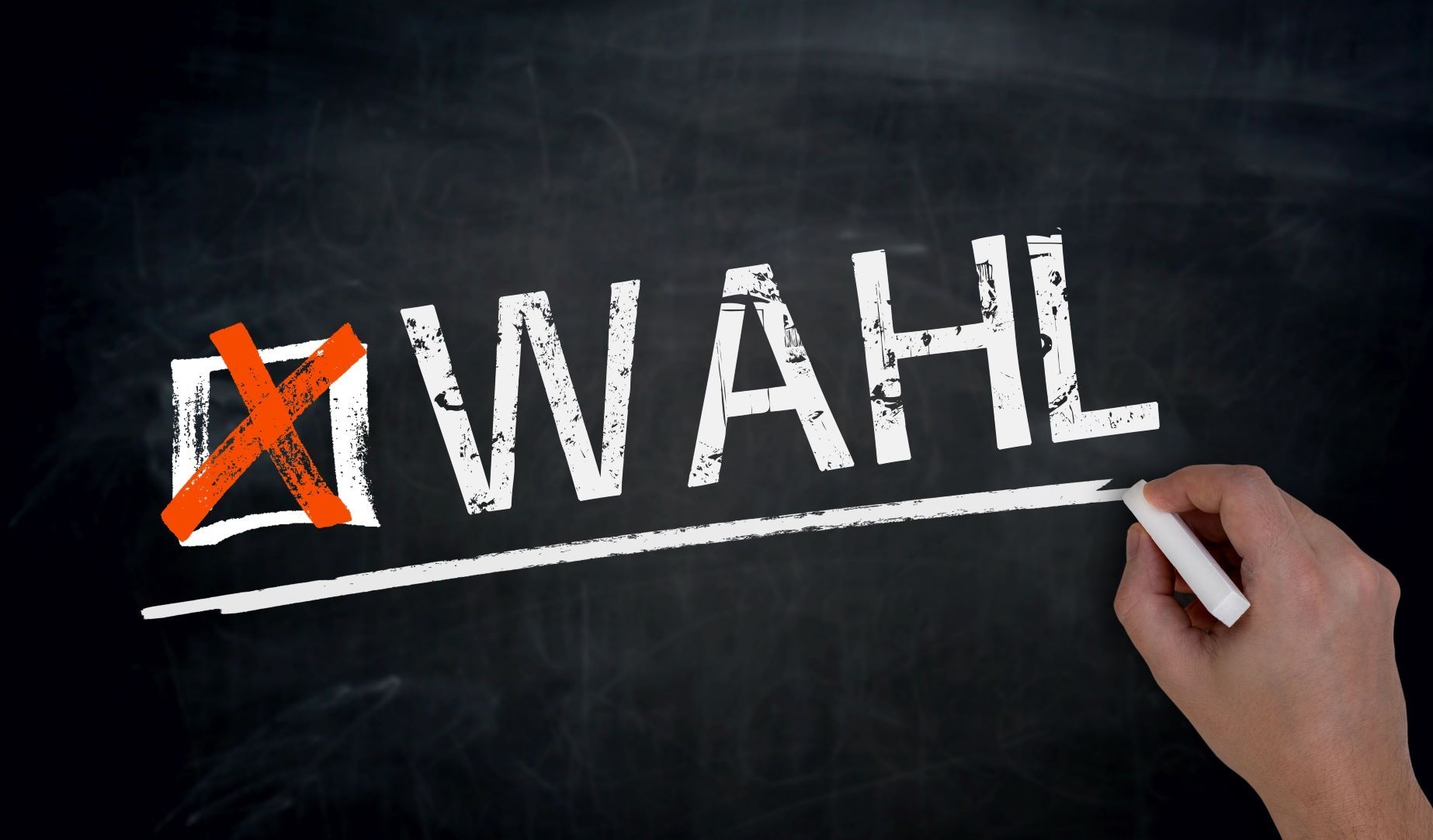 Eine Hand schreibt mit Kreide das Wort "Wahl" an eine dunkelgraue Schiefertafel