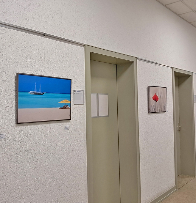 Ein Flur mir hellgrauen Türen und weißen Wänden, an den Wänden hängen mehrere gerahmte Farbfotografien