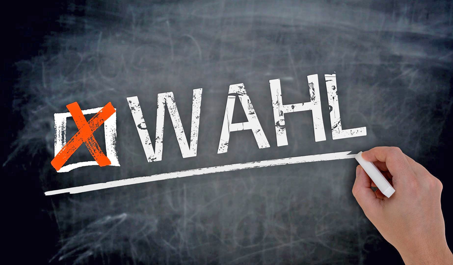 Eine Hand schreibt mit Kreide das Wort "Wahl" auf eine graue Oberfläche