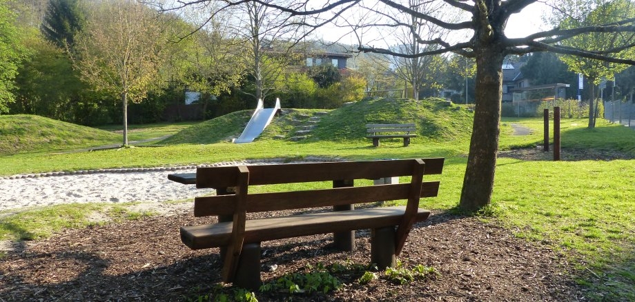 Blick auf einen Spielplatz mit einer Bank im Vordergrund